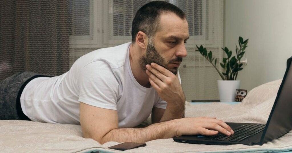 Man taking an online PTSD test while lying on his bed at home using a laptop.